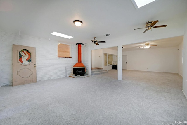 unfurnished living room featuring a wood stove, light carpet, ceiling fan, and brick wall