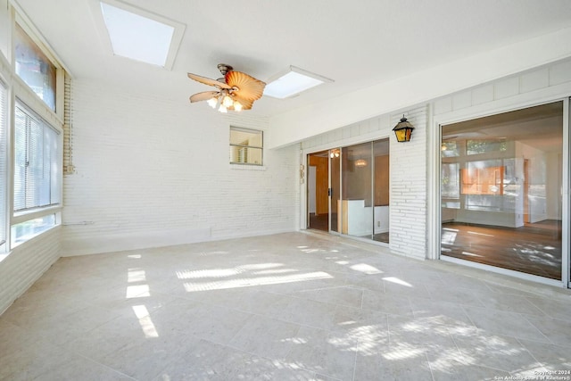 empty room featuring brick wall, a skylight, and ceiling fan