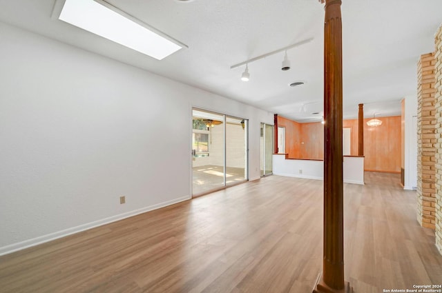 empty room featuring ornate columns, rail lighting, and light wood-type flooring