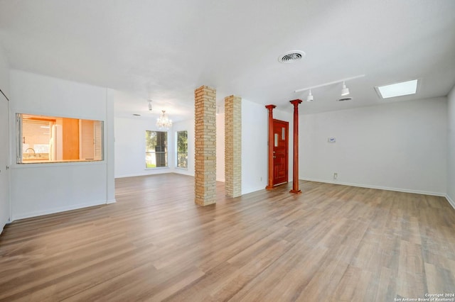 unfurnished living room featuring light wood-type flooring, a chandelier, decorative columns, and rail lighting