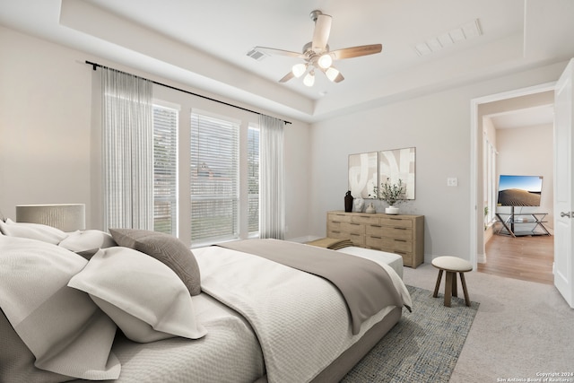 bedroom featuring light hardwood / wood-style floors, a tray ceiling, and ceiling fan