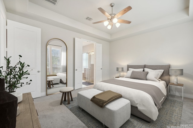 carpeted bedroom with a tray ceiling, ensuite bathroom, and ceiling fan