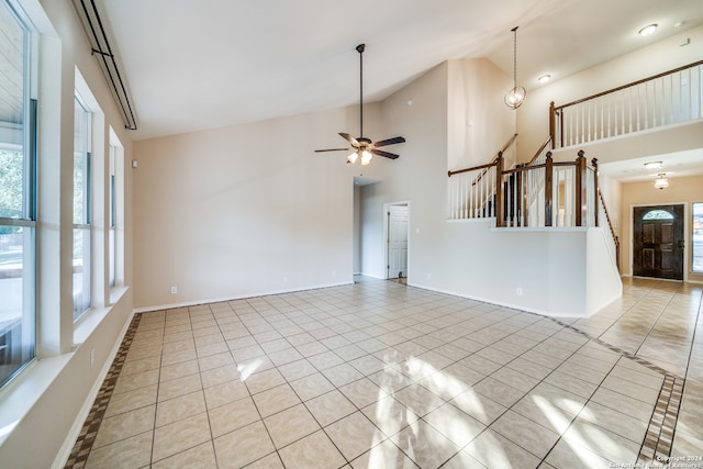 unfurnished living room featuring light tile patterned flooring, ceiling fan with notable chandelier, and high vaulted ceiling