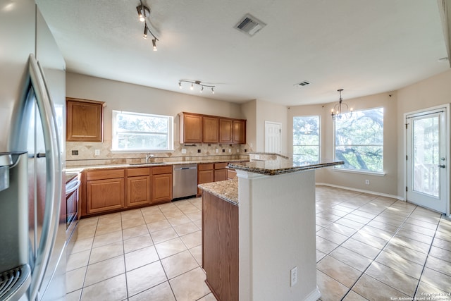 kitchen featuring decorative backsplash, a kitchen island, light stone counters, stainless steel appliances, and hanging light fixtures