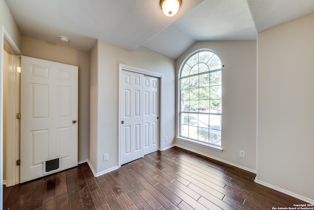 unfurnished bedroom featuring a textured ceiling, lofted ceiling, dark hardwood / wood-style floors, and a closet