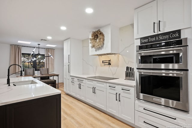 kitchen featuring black electric cooktop, light wood-type flooring, light stone countertops, white cabinets, and double oven