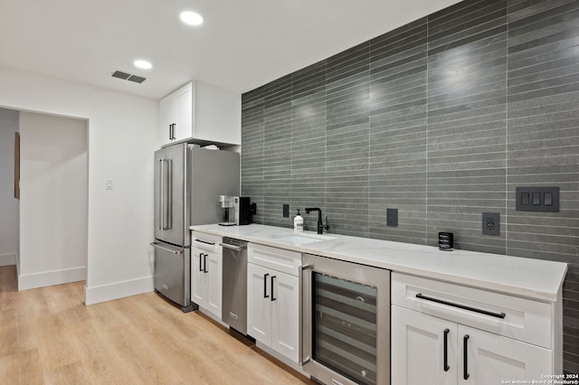 kitchen featuring stainless steel refrigerator, light wood-type flooring, beverage cooler, sink, and white cabinets