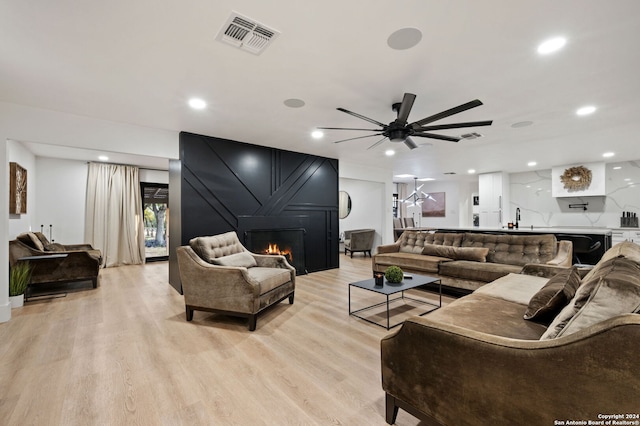 living room with ceiling fan, sink, a fireplace, and light hardwood / wood-style floors