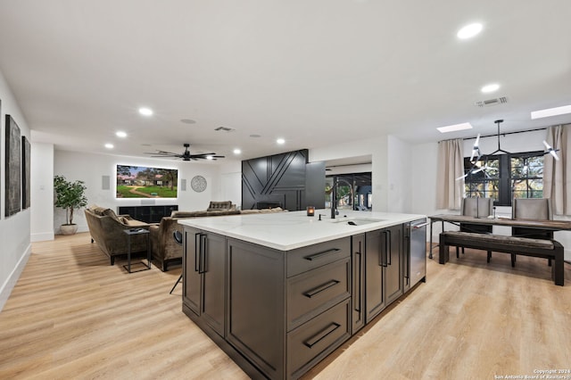 kitchen with a kitchen island with sink, light wood-type flooring, ceiling fan, sink, and dishwasher