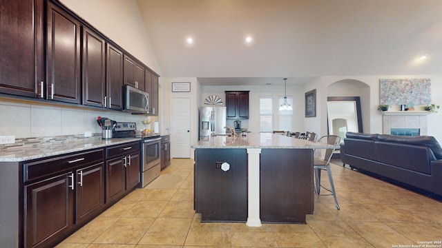 kitchen featuring a kitchen breakfast bar, vaulted ceiling, hanging light fixtures, appliances with stainless steel finishes, and an island with sink