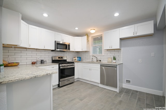 kitchen with white cabinets, light stone countertops, sink, stainless steel appliances, and light wood-type flooring