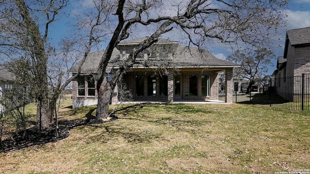 rear view of house with brick siding, a lawn, and fence