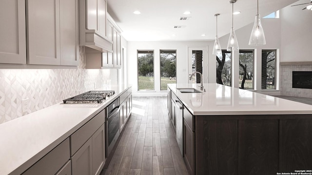 kitchen with an island with sink, a sink, stainless steel appliances, light countertops, and backsplash