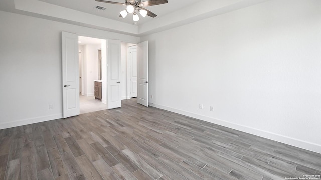 unfurnished bedroom with visible vents, ensuite bathroom, baseboards, and wood finished floors