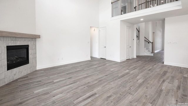 unfurnished living room featuring a fireplace, stairway, a high ceiling, wood finished floors, and baseboards