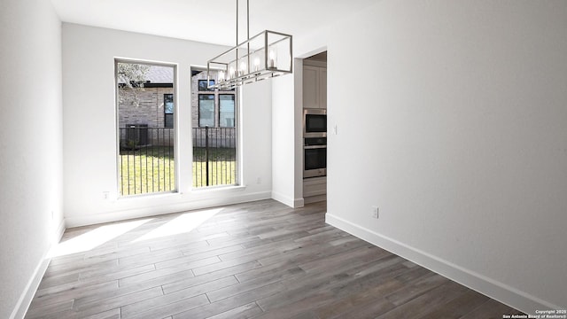 unfurnished dining area with a chandelier, dark wood-type flooring, and a wealth of natural light