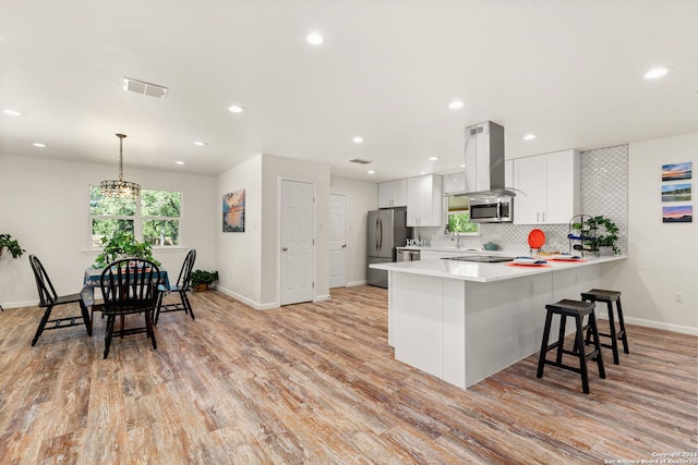 kitchen with white cabinets, kitchen peninsula, pendant lighting, appliances with stainless steel finishes, and island exhaust hood