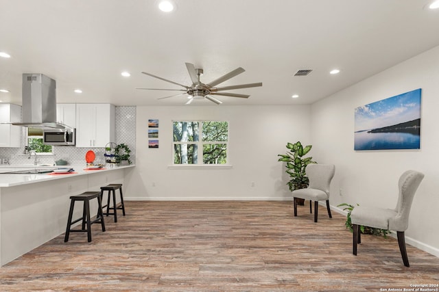 interior space with light hardwood / wood-style flooring, decorative backsplash, a kitchen bar, island range hood, and white cabinetry