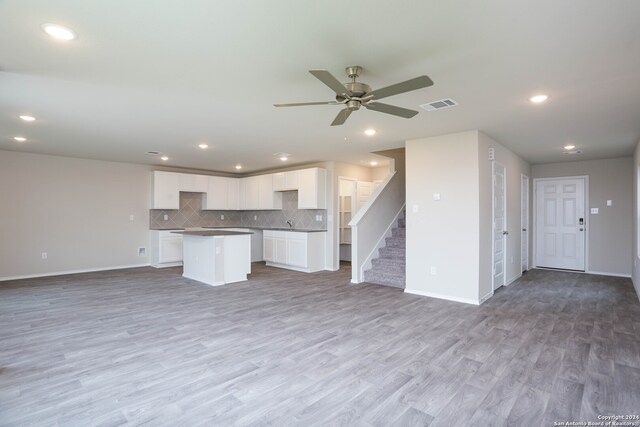 kitchen featuring light wood-type flooring, ceiling fan, a center island, tasteful backsplash, and white cabinetry