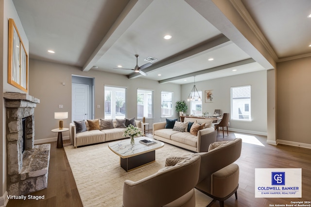 living room with beam ceiling, wood-type flooring, a stone fireplace, and plenty of natural light