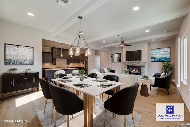 dining space featuring beamed ceiling, ceiling fan, a fireplace, and light wood-type flooring