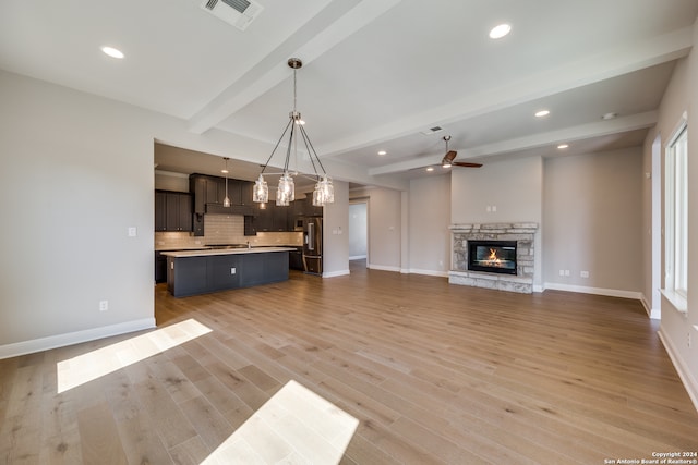 unfurnished living room with beamed ceiling, ceiling fan, a fireplace, and light hardwood / wood-style floors