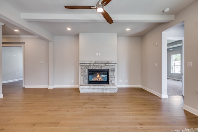 unfurnished living room featuring beamed ceiling, a stone fireplace, ceiling fan, and light hardwood / wood-style flooring