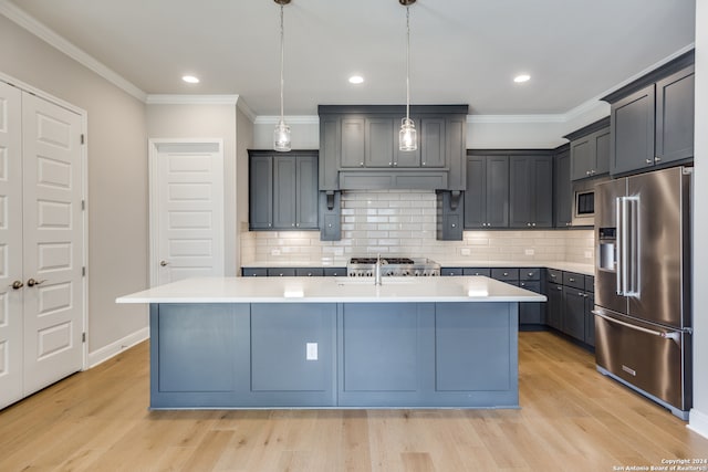 kitchen with sink, hanging light fixtures, stainless steel appliances, ornamental molding, and an island with sink