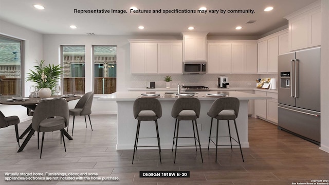 kitchen with appliances with stainless steel finishes, dark wood-type flooring, an island with sink, and white cabinets