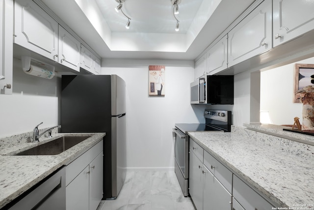 kitchen featuring light stone counters, a raised ceiling, sink, white cabinetry, and appliances with stainless steel finishes