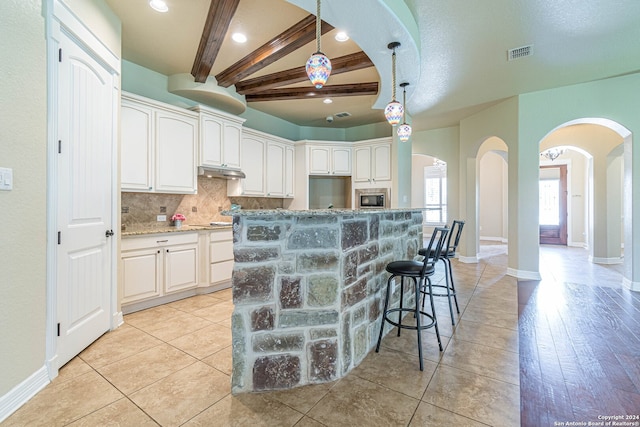 kitchen with light wood-type flooring, beam ceiling, a kitchen island, stainless steel microwave, and white cabinetry