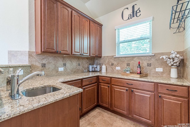 kitchen with pendant lighting, tasteful backsplash, vaulted ceiling, sink, and light stone countertops