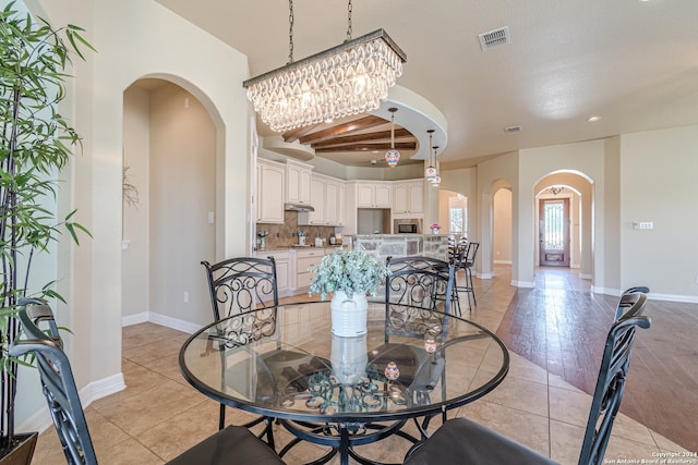 dining space featuring beamed ceiling, a notable chandelier, light hardwood / wood-style floors, and a textured ceiling