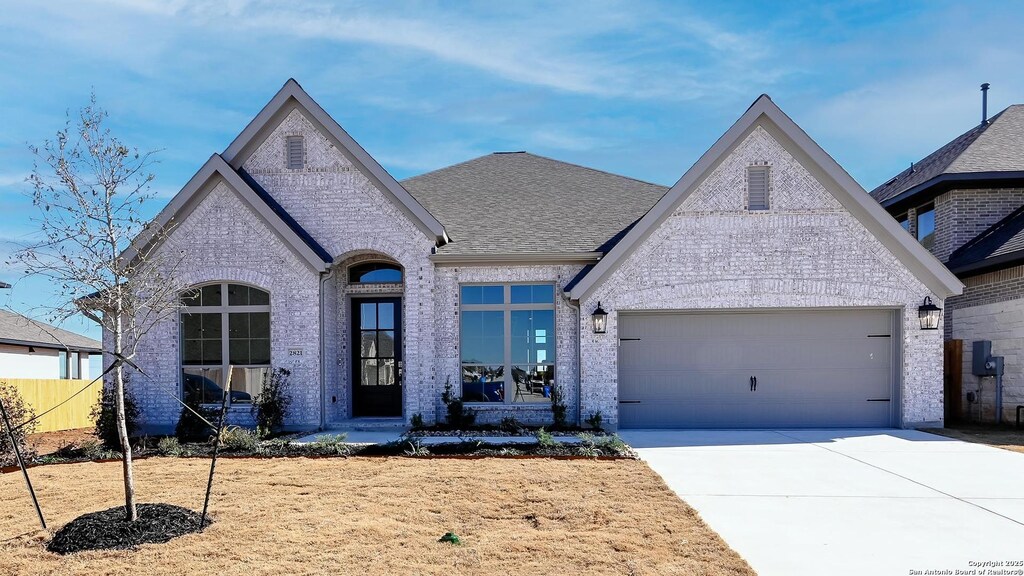 french country home featuring a garage, brick siding, and driveway