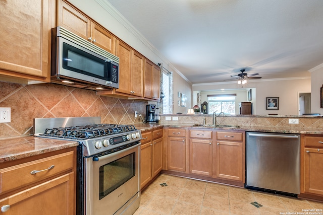 kitchen with light stone counters, ceiling fan, stainless steel appliances, sink, and crown molding