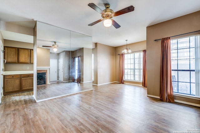 unfurnished living room featuring ceiling fan with notable chandelier, light hardwood / wood-style floors, and a tile fireplace