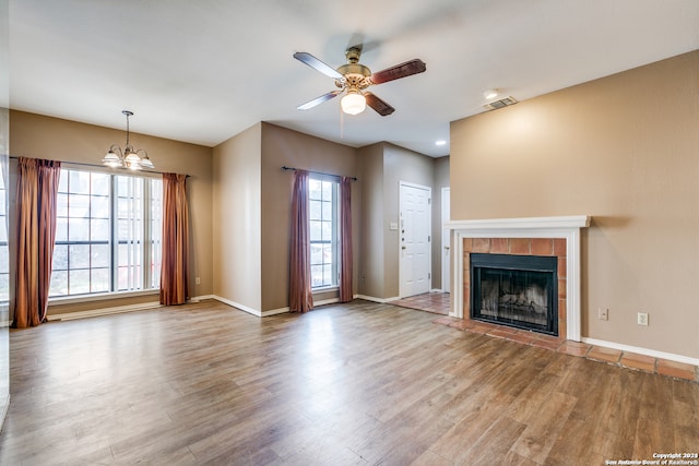 unfurnished living room with ceiling fan with notable chandelier, a fireplace, and hardwood / wood-style floors