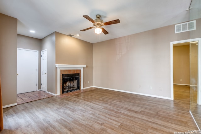 unfurnished living room with ceiling fan, a tile fireplace, and light hardwood / wood-style flooring