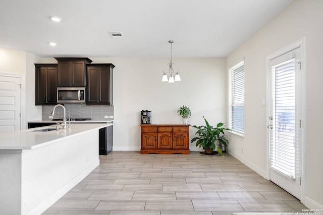 kitchen with dark brown cabinetry, hanging light fixtures, a notable chandelier, sink, and backsplash