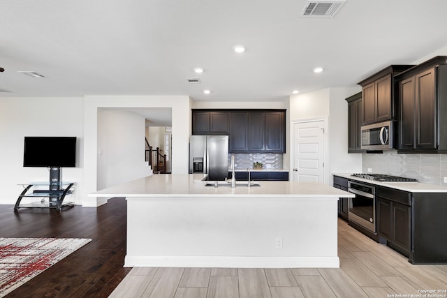 kitchen with backsplash, light hardwood / wood-style flooring, sink, stainless steel appliances, and an island with sink