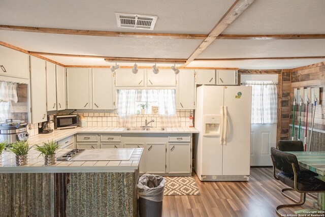 kitchen featuring beam ceiling, tasteful backsplash, wood-type flooring, white fridge with ice dispenser, and gas stovetop