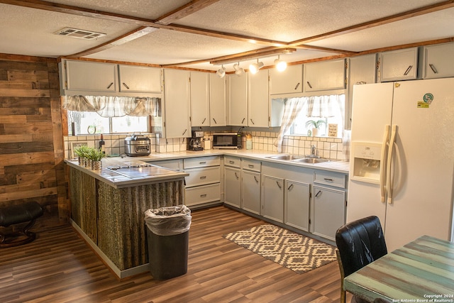 kitchen with white refrigerator with ice dispenser, dark wood-type flooring, sink, wood walls, and a textured ceiling