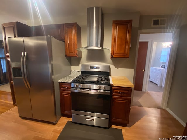 kitchen with appliances with stainless steel finishes, wall chimney range hood, and light hardwood / wood-style flooring