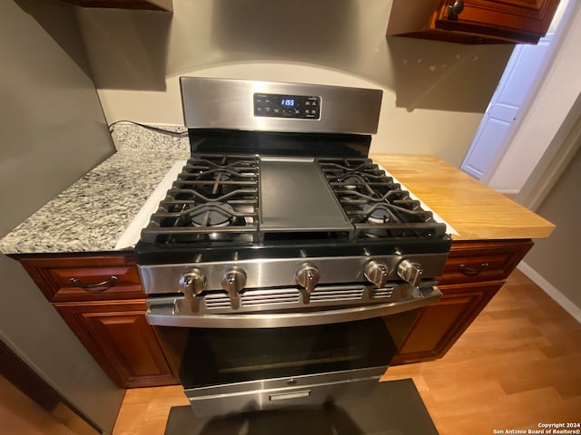 interior details featuring light stone countertops, stainless steel gas stove, and light hardwood / wood-style flooring