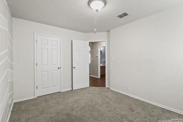 unfurnished bedroom with a textured ceiling and dark colored carpet