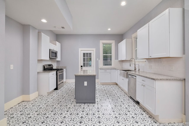 kitchen featuring a center island, sink, stainless steel appliances, light stone counters, and white cabinets