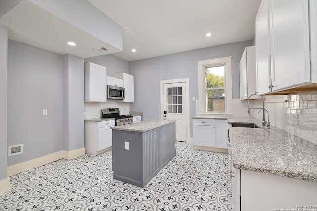 kitchen with white cabinets, light stone counters, a kitchen island, and stainless steel appliances