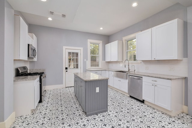 kitchen with white cabinets, light stone countertops, a kitchen island, and appliances with stainless steel finishes