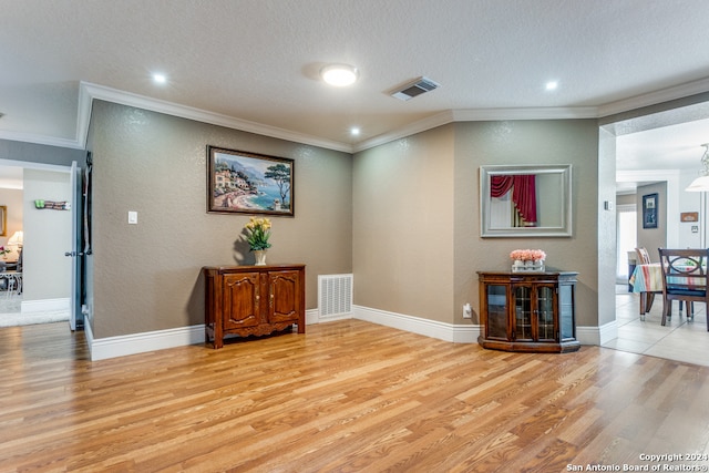 interior space featuring light wood-type flooring, crown molding, and a textured ceiling