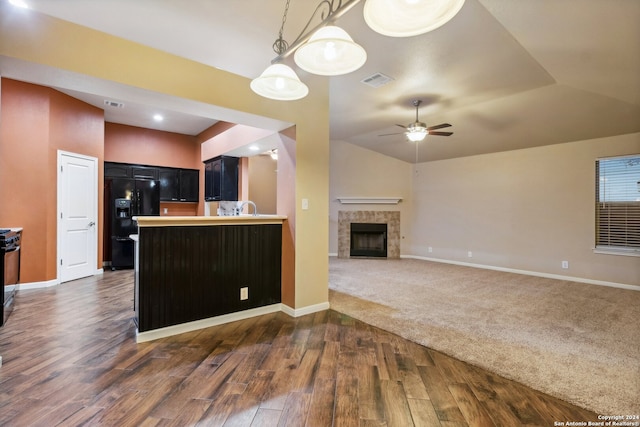 kitchen with lofted ceiling, black refrigerator with ice dispenser, dark colored carpet, kitchen peninsula, and a tiled fireplace